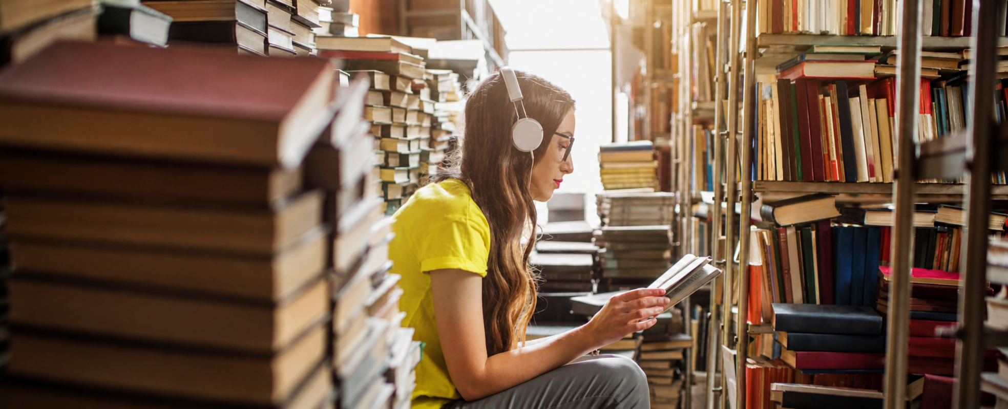 Élève écoutant de la musique au casque en lisant dans une bibliothèque